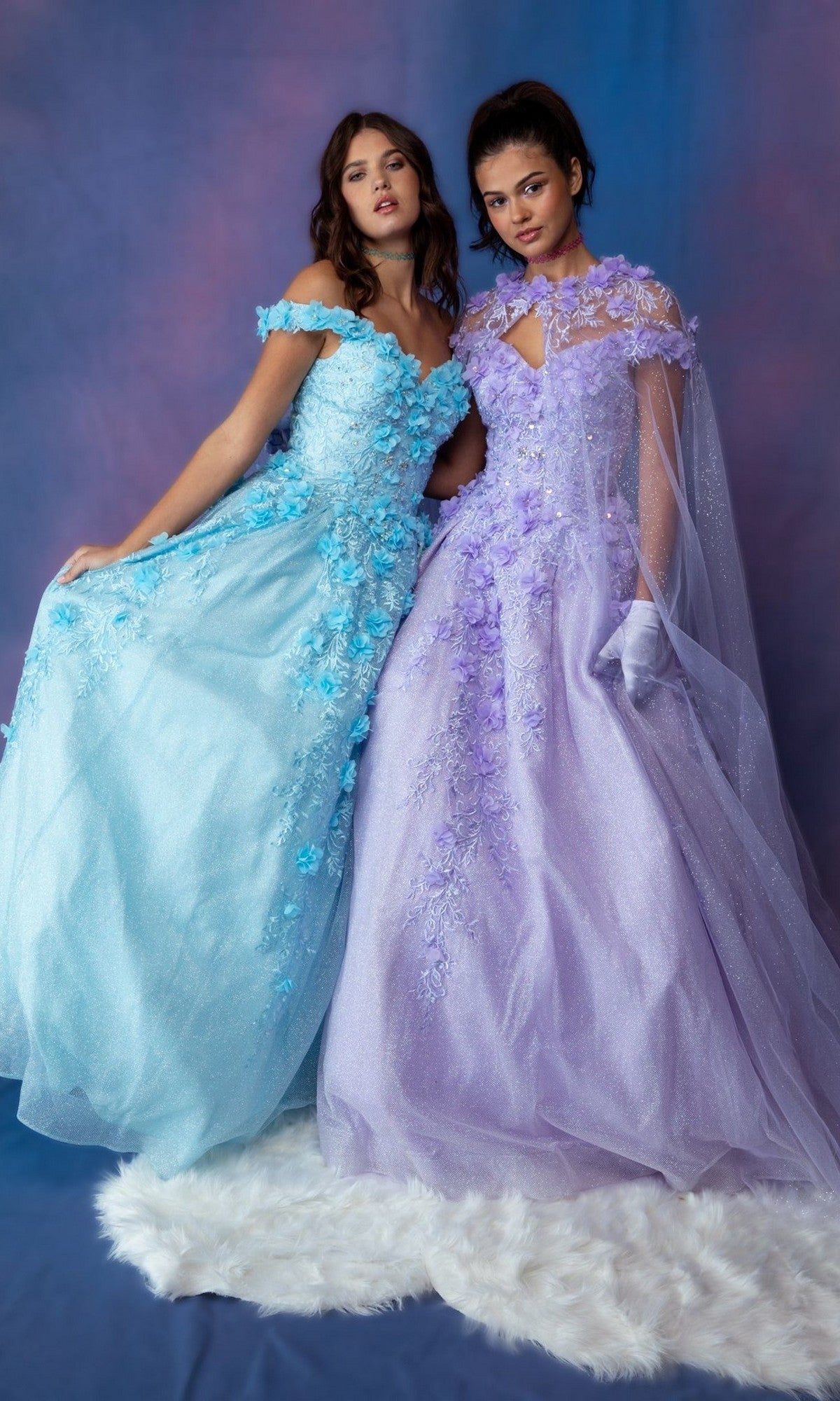 Two women wear Eureka 9339 long prom dresses—one in light blue glitter, the other in lavender with 3D floral appliques—standing on a white fur rug against a blue and purple backdrop.